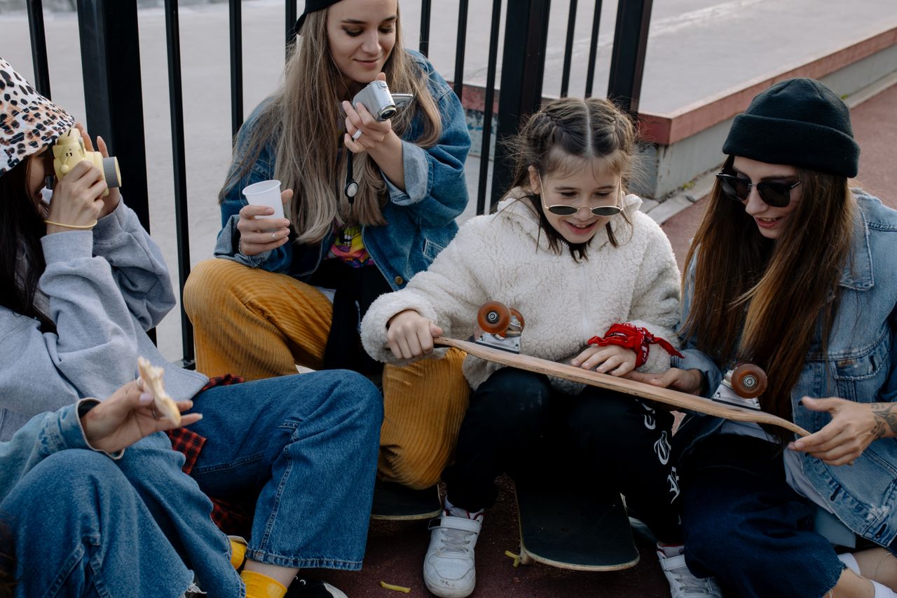 Group of teenage girls hanging out with skateboards outdoors in a casual urban environment.