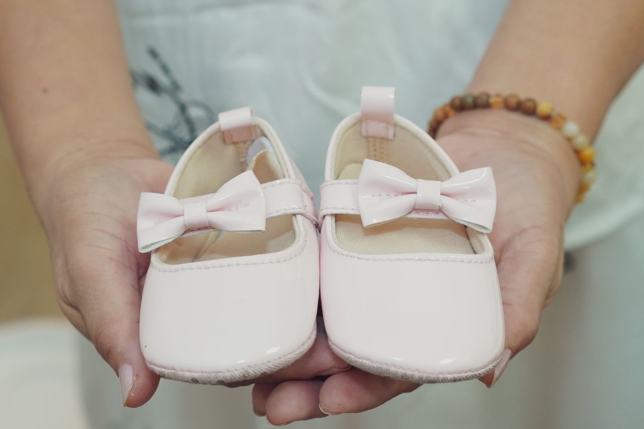 Adorable baby shoes with bows held in hands, perfect for a baby girl announcement or gift idea.