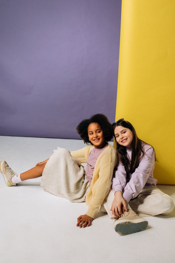 Two young girls sitting and smiling against a vibrant, colorful background.